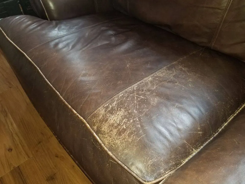Worn leather cushion edge showing friction scuffing before repair